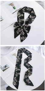 Detail of black floral silk scarf tied in a bow and displayed flat on a white table
