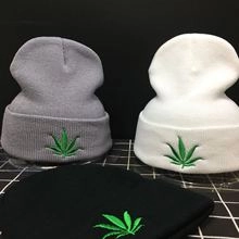 Detail showing embroidered green leaf on grey, white, and black knit beanies