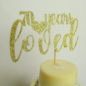 Close-up of golden glitter 70 Years Loved cake topper for wedding anniversary party