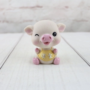 Gros plan d'une figurine de cochon en résine rose avec bavoir jaune et détail gravé