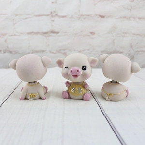 Détail de trois figurines de cochons en résine, dont un clin d'œil, sur bois