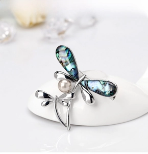 Detail of silver dragonfly brooch featuring colorful abalone shell wings and white pearl