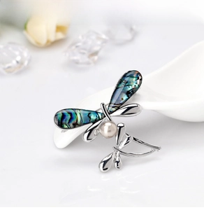 Close-up of dragonfly brooch with colorful abalone shell wings and a white pearl center