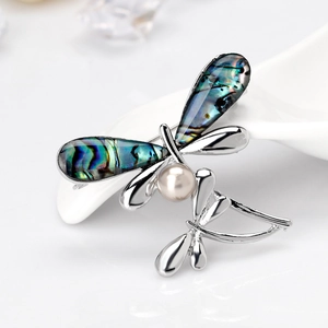 Elegant dragonfly brooch with abalone shell wings and white pearl on a ceramic stand