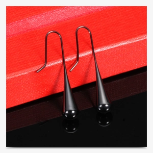 Macro shot of long black teardrop earrings on red textured box with mirror reflections