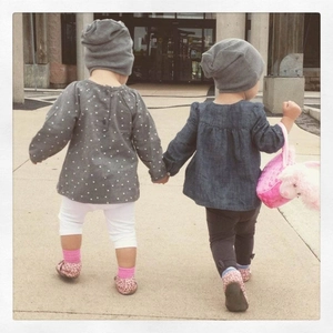 Outdoor shot of two toddlers wearing casual cotton beanies and autumn outfits from behind