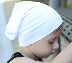 Close-up of a soft white cotton knit beanie for kids worn by a child in natural light