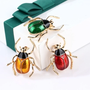Detailed view of colorful enamel beetle brooches in gift packaging with green ribbons