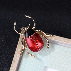 Detail of red beetle enamel brooch with glitter finish and golden legs on a frame