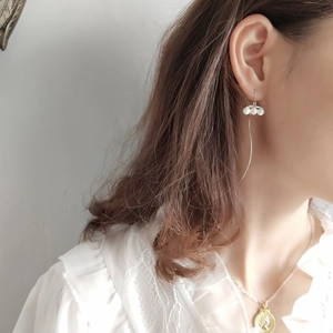 Detail of silver long curved ear threaders with triple white pearls worn by a model