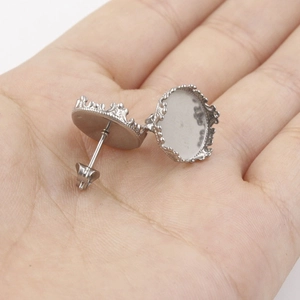 Crown-shaped stainless steel earring posts with round bezel cups shown on palm