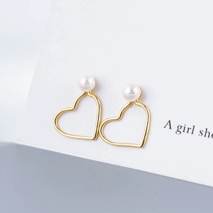 Close-up of gold hollow heart earrings with white pearls on a minimalist white card