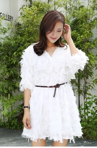 Detail of a slim brown leather belt cinching a white fringed dress on a fashion model