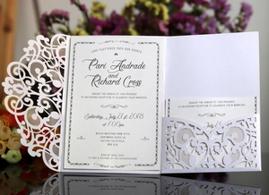 Detail of white laser-cut wedding invitation showing intricate lace patterns and card inserts