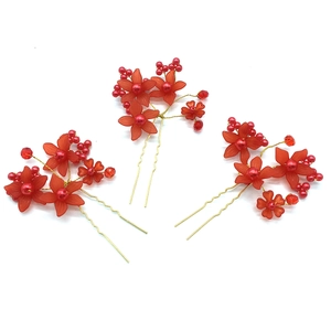 Detailed shot of three red matte flower hair pins with gold wire and pearl beads