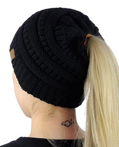 Close-up of black cable knit ponytail beanie showing the elastic top opening on a model