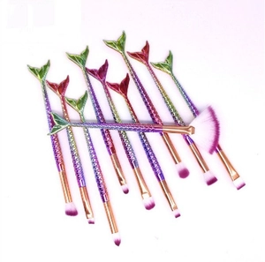 Flat lay of 10 gradient mermaid makeup brushes with purple bristles on soft purple background