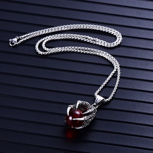 Détail d'un pendentif en forme de griffe de dragon argentée tenant une perle rouge
