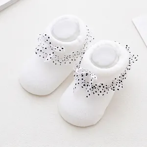 Detail of white infant socks with lace frill and polka dot bow on knitted fabric