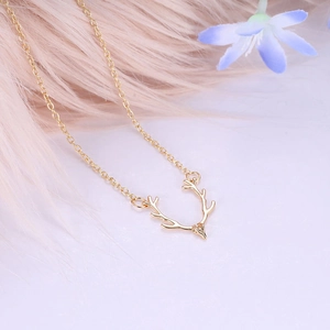 Elegant gold reindeer antler pendant necklace displayed on soft pink feathers and a blue flower