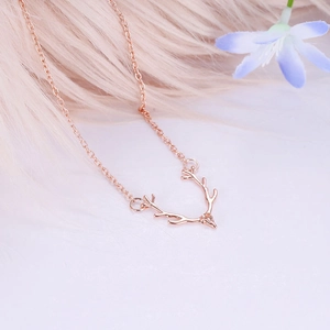 Close-up of rose gold reindeer antler pendant on soft pink plush background with blue flower