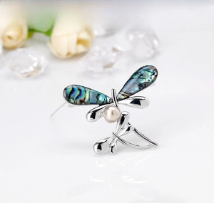 Macro detail of dragonfly brooch with iridescent wings and a central white pearl