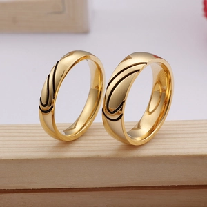 Golden titanium steel heart couple rings with black streamlined enamel on wooden surface