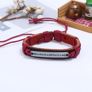 Détail du bracelet en cuir tressé rouge avec plaque en métal gravée d'un proverbe