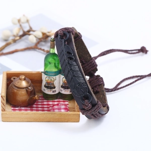 Braided brown leather bracelet featuring a black metal feather charm on a white background