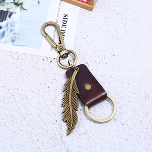 Vintage bronze feather keychain with dark brown leather strap on white background