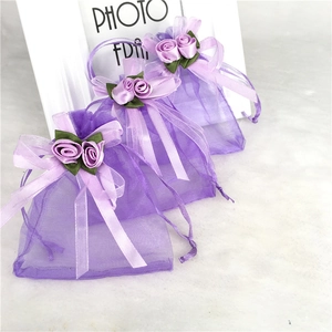 Three purple organza gift bags with ribbon roses on a white marble surface