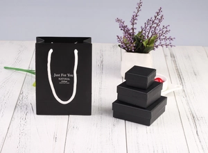 Elegant black jewelry gift box set with 'Just For You' shopping bag on white wood surface