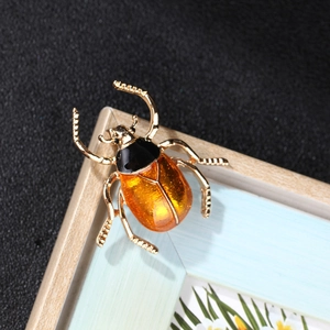 Close-up of enamel beetle brooch with orange translucent resin and gold glitter inlay