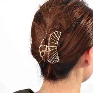 Rear view of gold hollow shell metal hair claw clip holding hair on white background