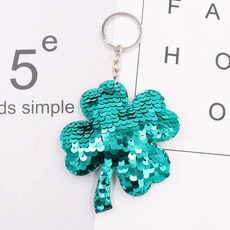Macro shot of turquoise sequin four-leaf clover keychain with metallic keyring on paper
