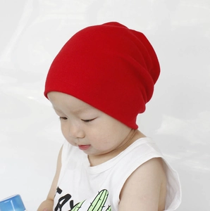 Close-up of baby wearing a bright red soft cotton knitted beanie hat for autumn and winter