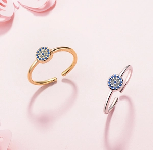 Detailed view of silver and gold evil eye rings with blue zircon inlay on pink background