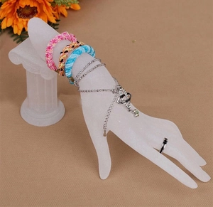 Modello di mano bianca opaca che mostra vari braccialetti e un anello su sfondo decorativo