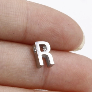 Detailed close-up of a silver stainless steel letter R bead held between fingers