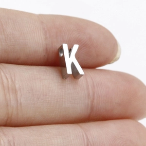 Close-up of a polished stainless steel letter K charm held by hand for jewelry DIY