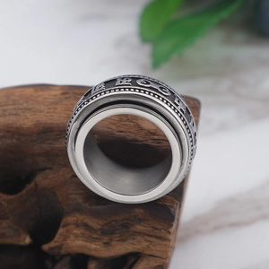 Spinning silver stainless steel ring with embossed religious mantra on wooden stand