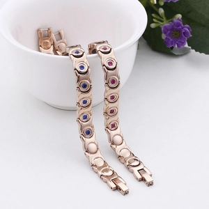 Rose gold magnetic therapy bracelets with blue and pink rhinestones on a ceramic bowl