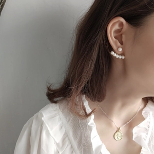 Detail of model wearing fan-shaped pearl earrings and a vintage gold coin necklace