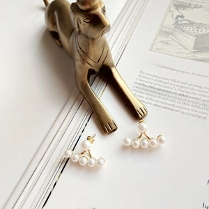 Detail of fan-shaped gold pearl earrings resting on vintage book with dog sculpture