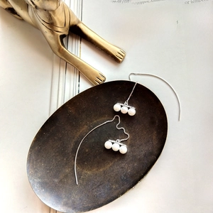 Artistic detail of 925 silver long thread earrings with three pearls on a metal plate