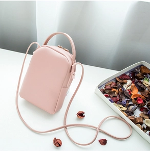 Pink mini PU leather crossbody phone bag on a white table with decorative dried flowers
