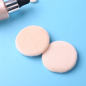 Detail view of two soft round cotton powder puffs in apricot color on a blue background