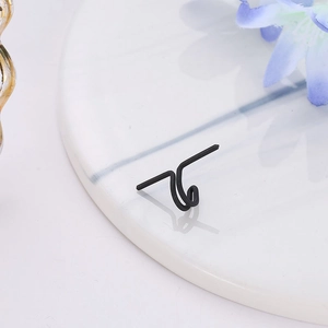 Detailed view of a minimalist black U-shaped double hoop clip earring on white marble