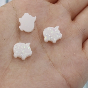 Close-up of three iridescent white opal pig charms for DIY jewelry making and nail art