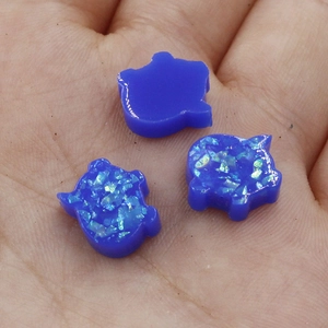 Macro shot of three blue pig-shaped synthetic opal beads held in a palm showing shimmer